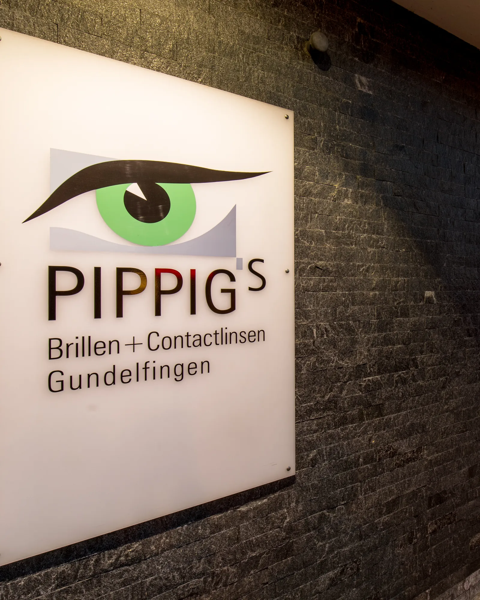 Das beleuchtete Firmenschild mit dem grünen Auge an der Außenwand